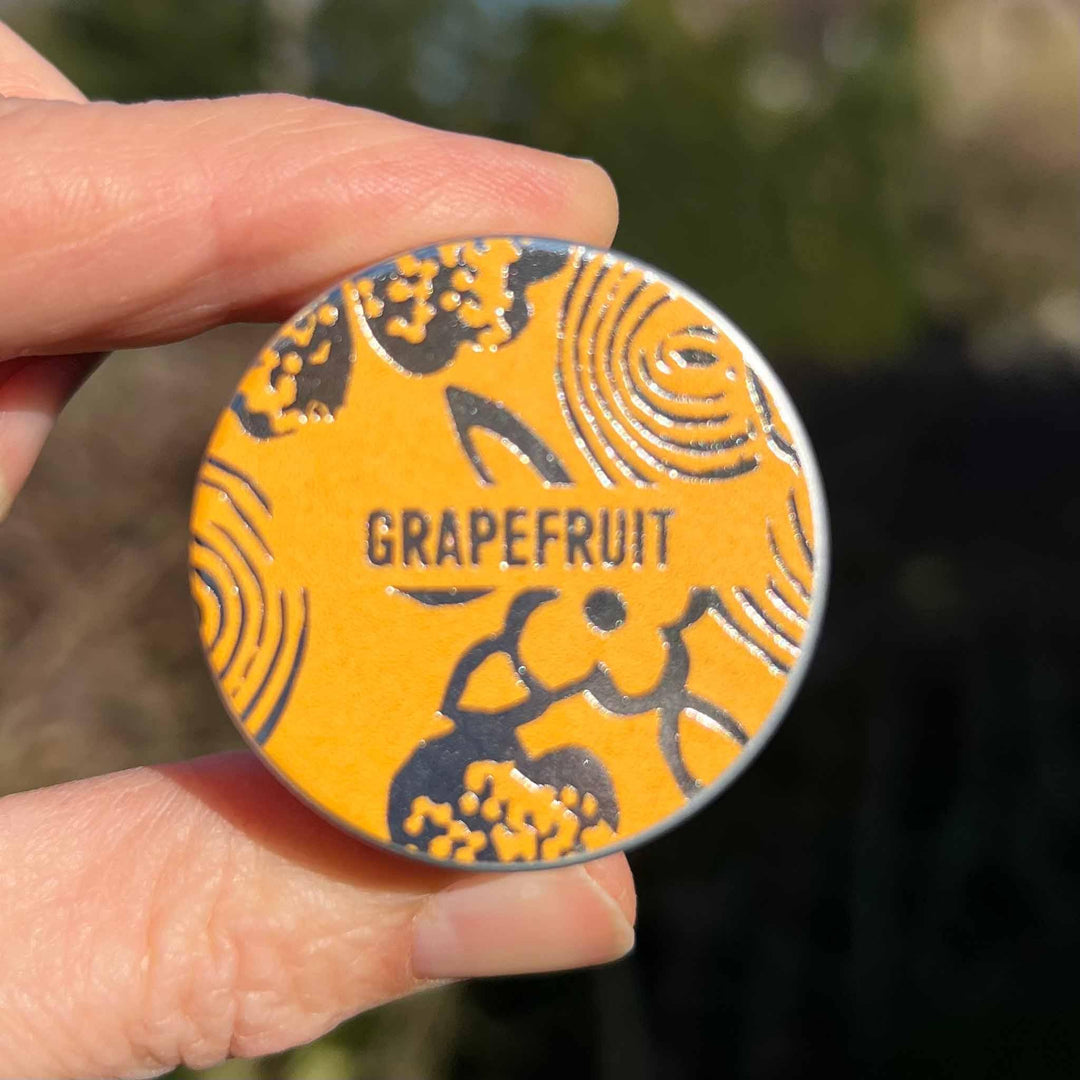 Hand holding Grapefruit lip balm tin to show sizing