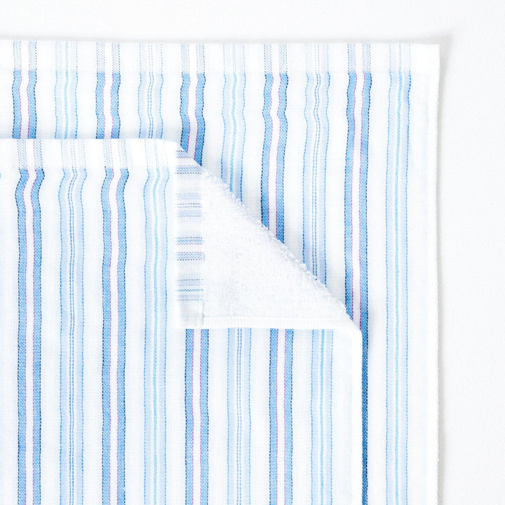 Close up of a striped towel with tones of blue, folded down on one corner to show the soft terry pile on the reverse of the towel.
