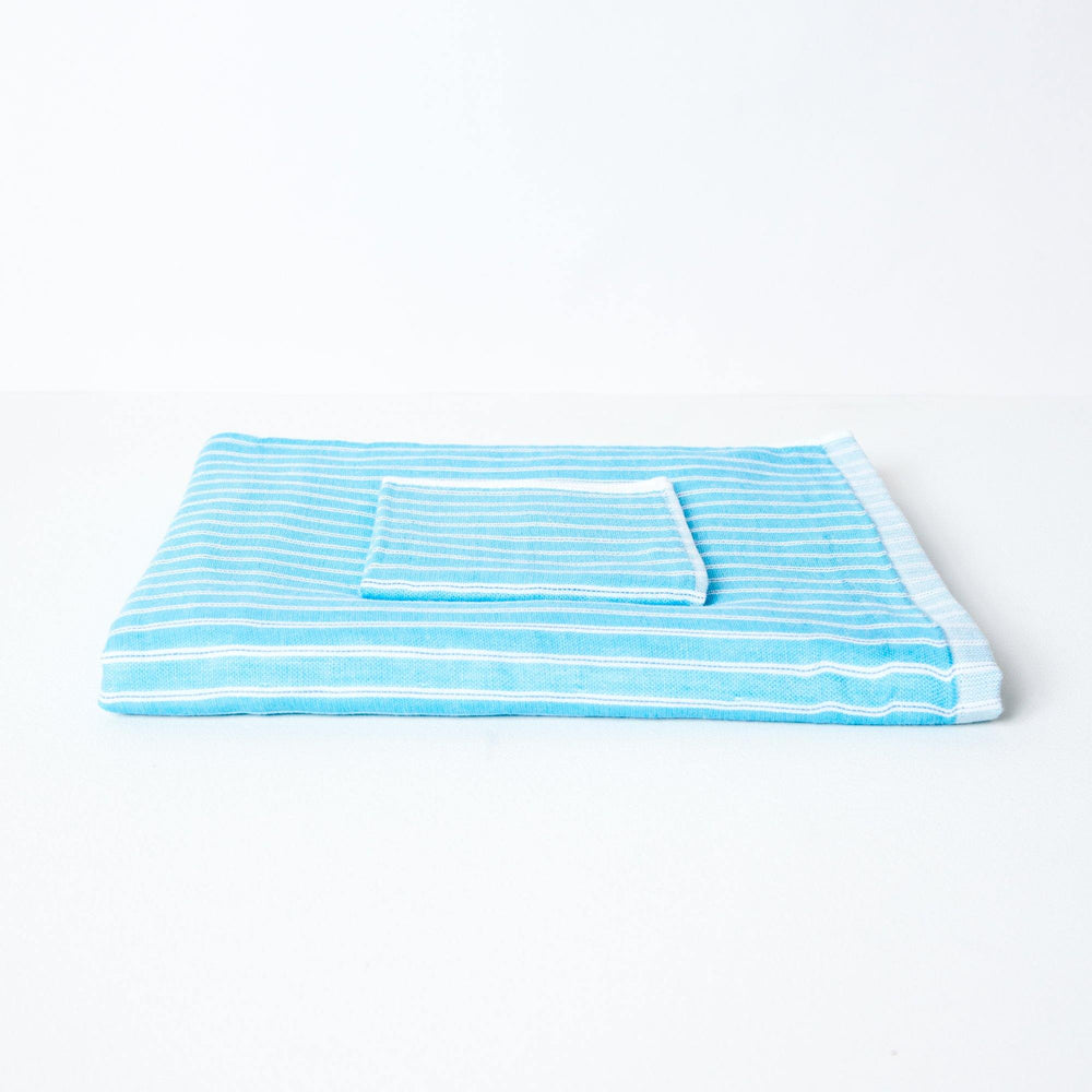 A striped towel with turquoise and white stripes, neatly folded with a coordinating flannel on top.