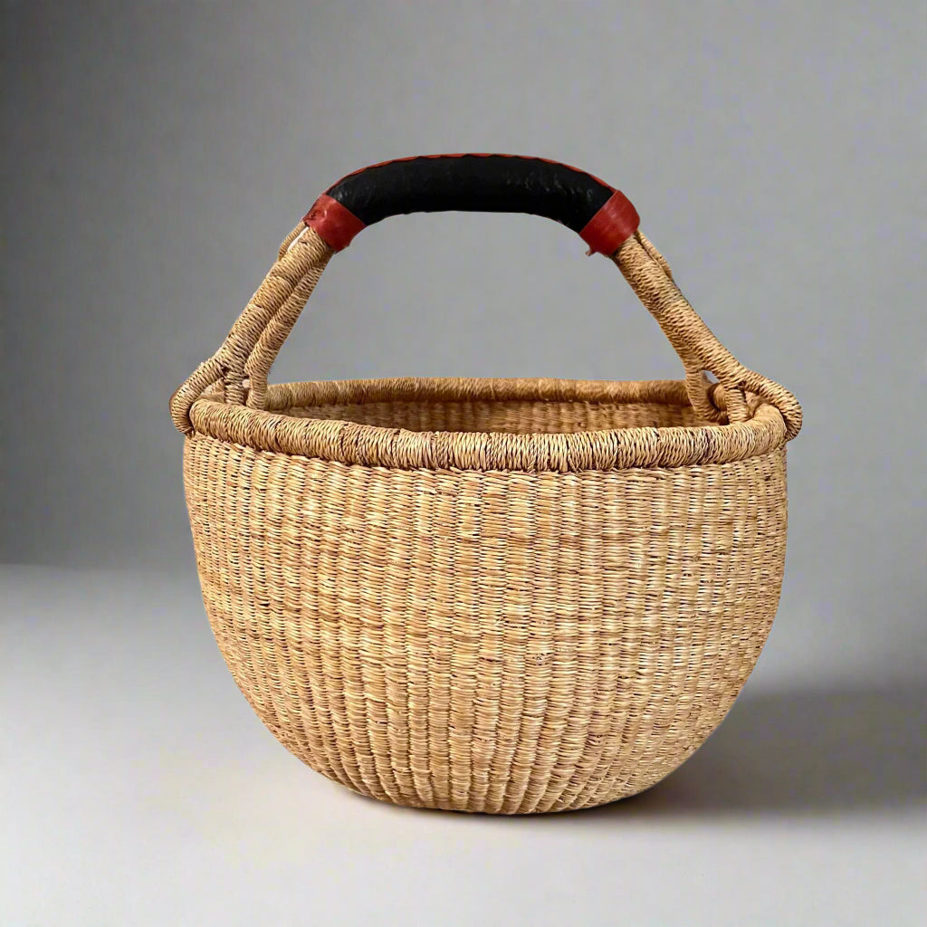 Round basket in neutral colours with black and tan handles, in studio setting