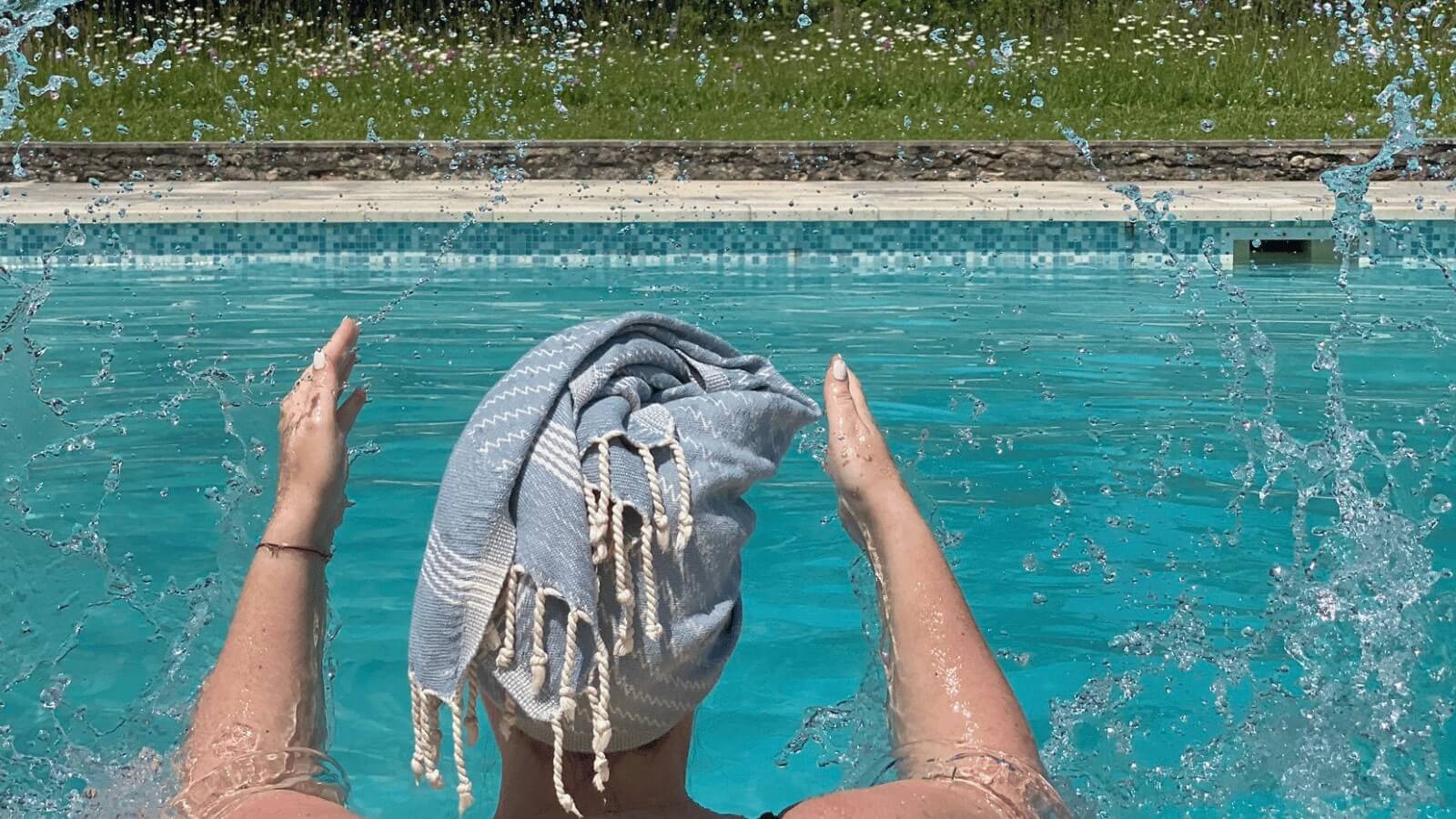 Lady splashes water in swimming pool wearing a pale blue hair towel