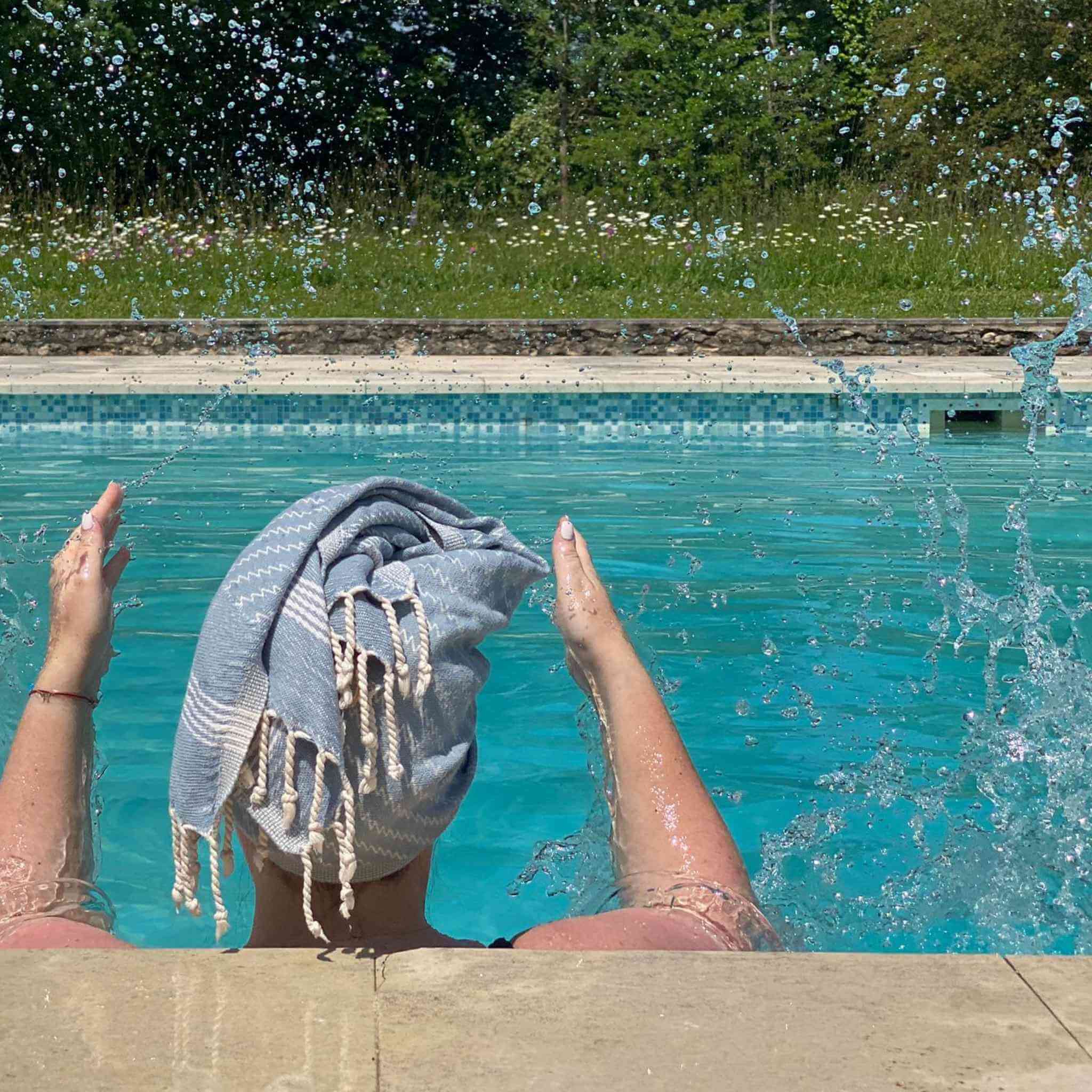 Lady splashes water in swimming pool wearing a pale blue hair towel