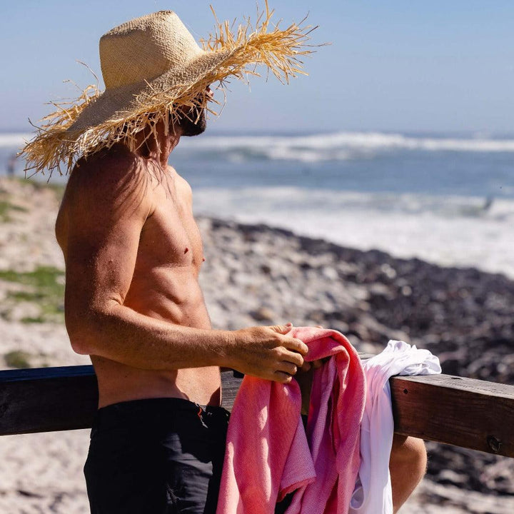 Man looking out to sea with large straw sunhat and coral Dune beach towel