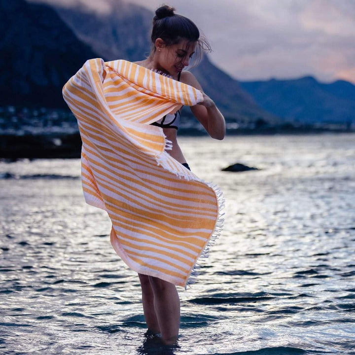Lady in the water wrapping herself in a large apricot and white stripe towel 