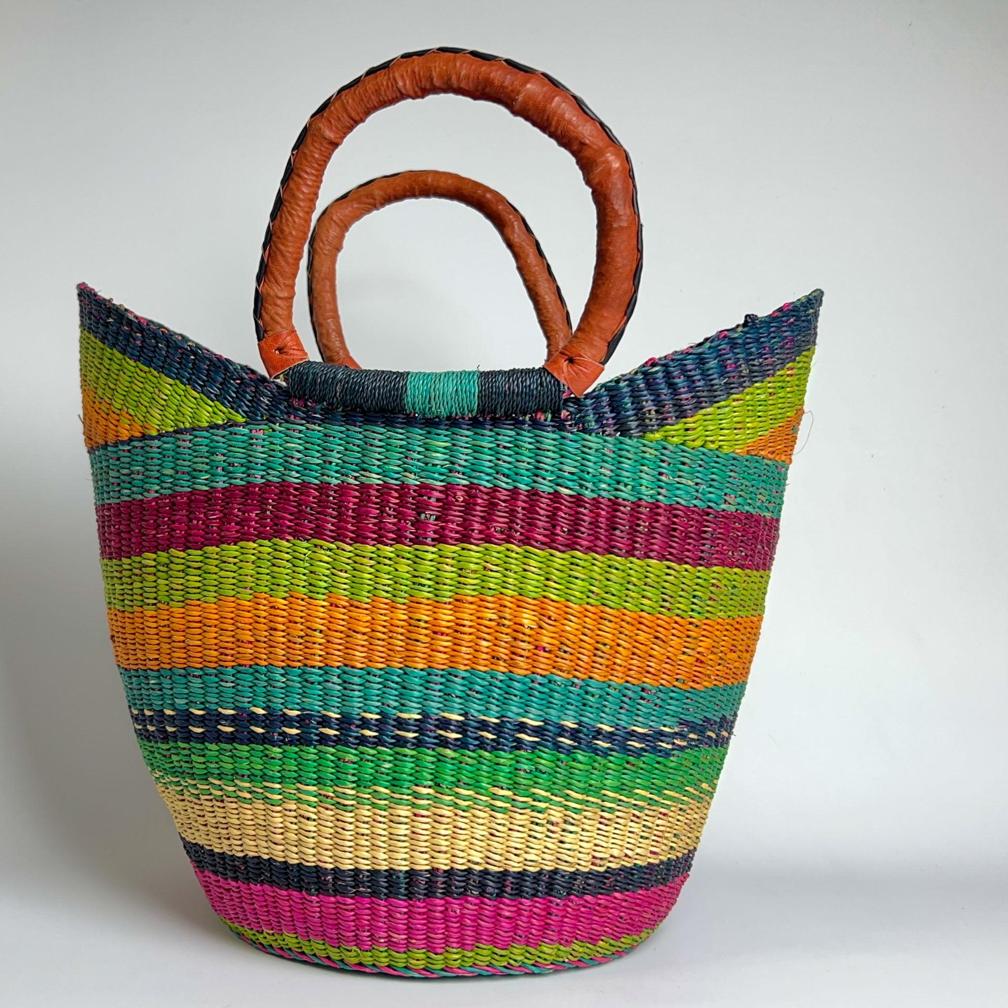 Close up of a traditional U Shopper basket in bright colours of pink, green, blues and orange, complete with leather handles.  
