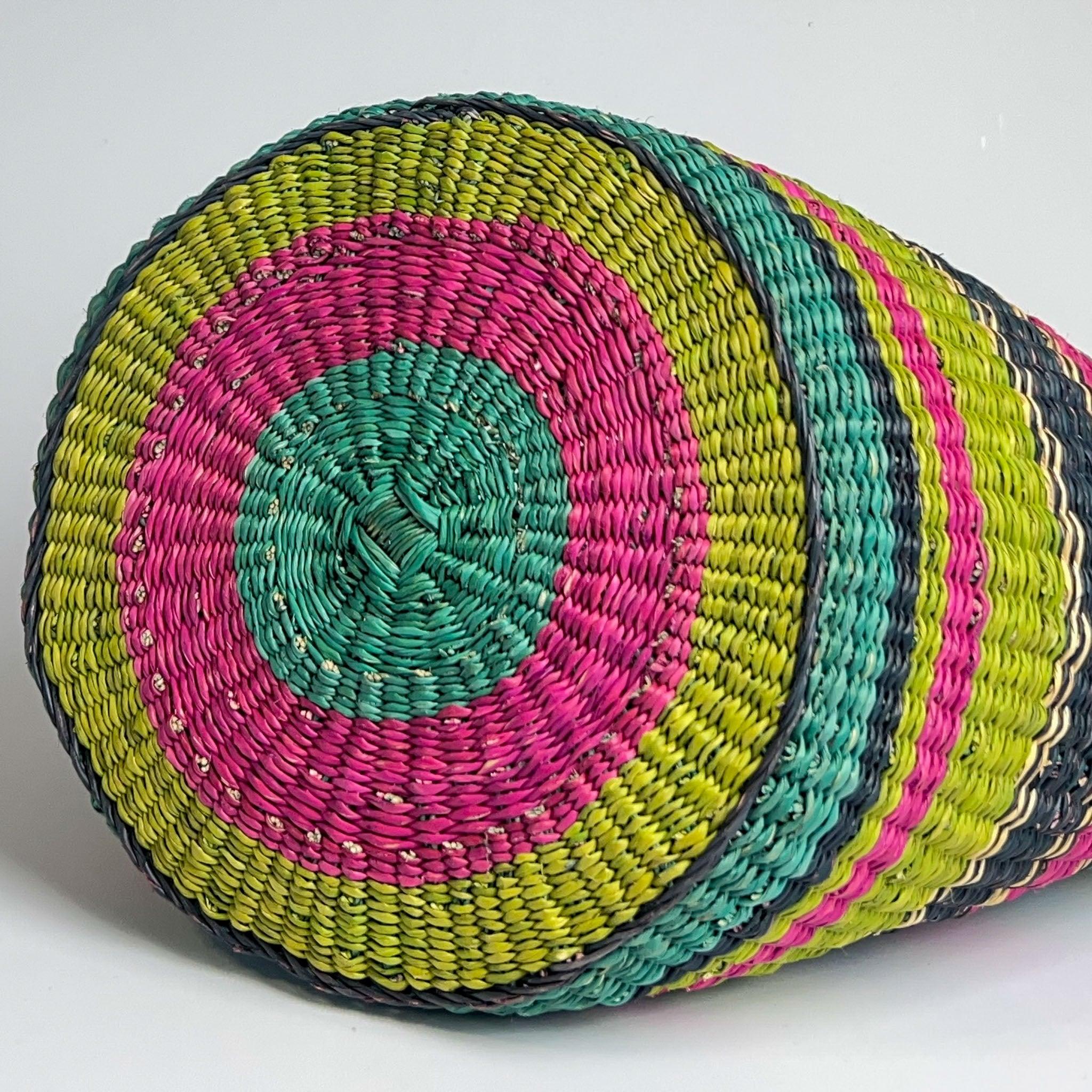 African shopper basket on it's side showing off a circular stripe design in bright pink, blue and lime green.