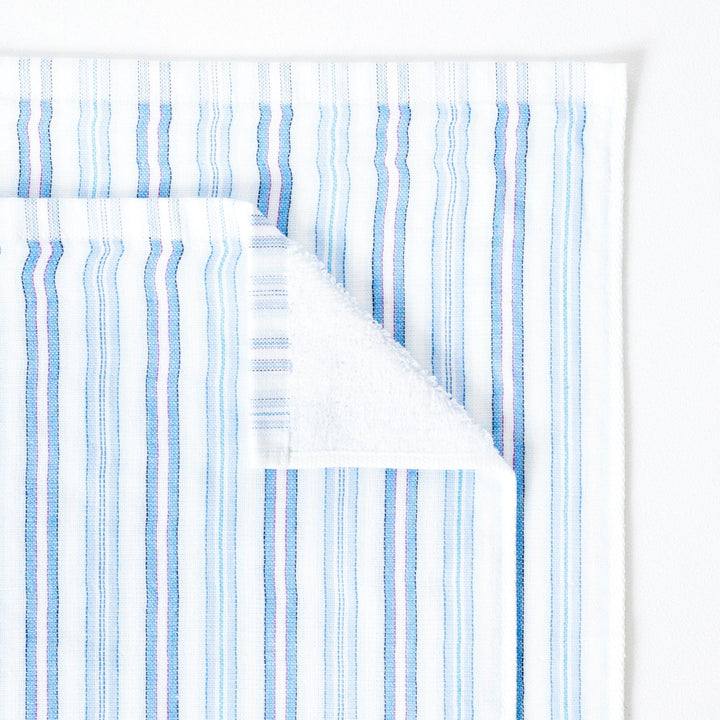 Close up of a striped towel with tones of blue, folded down on one corner to show the soft terry pile on the reverse of the towel. 