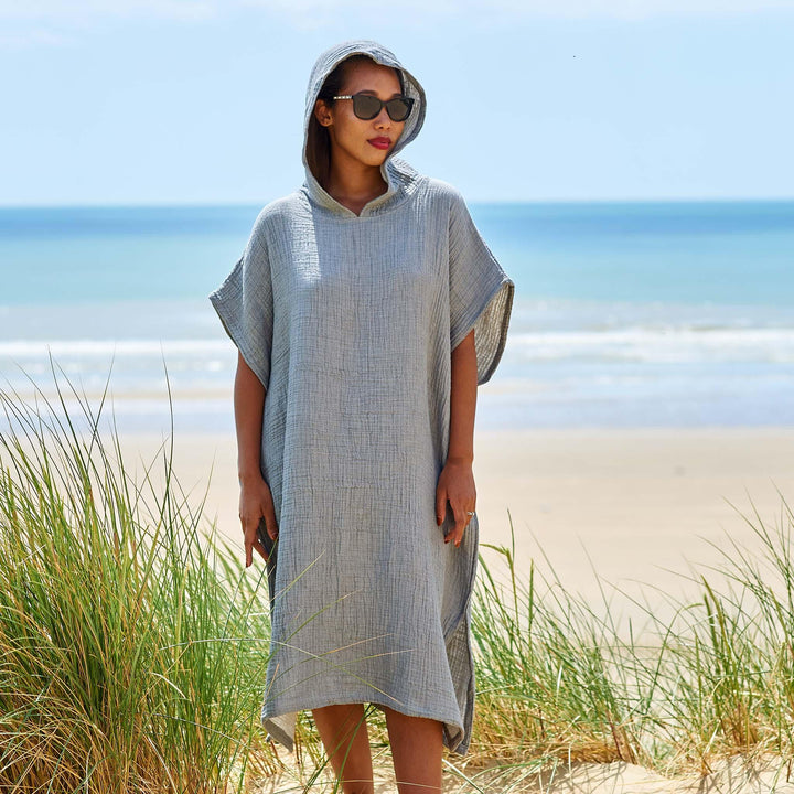 A woman at the beach wearing a light grey soft muslin cotton hooded beach changing robe in grey.