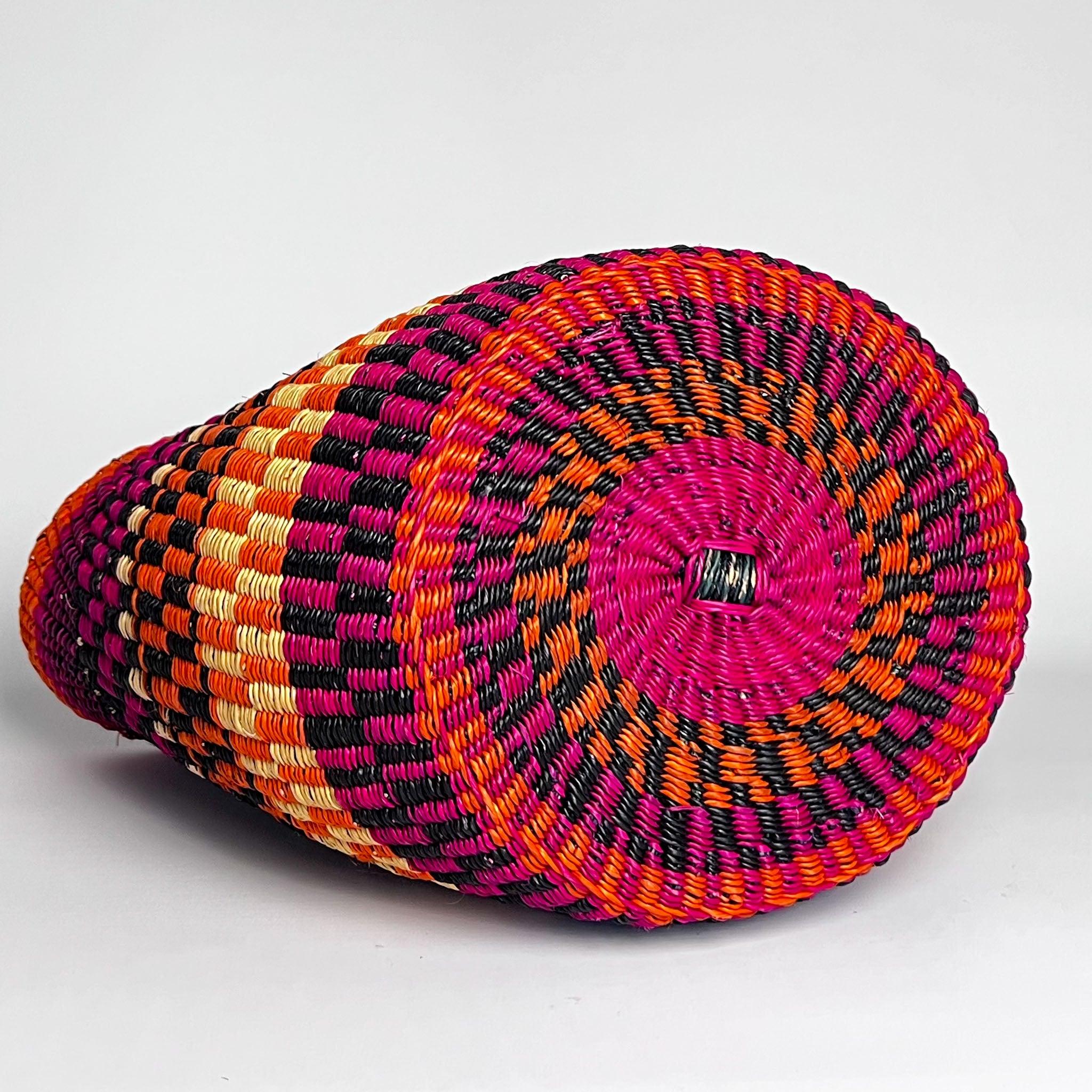 African basket on it's side showing the attractive design woven on the base, in pink, blue and orange.