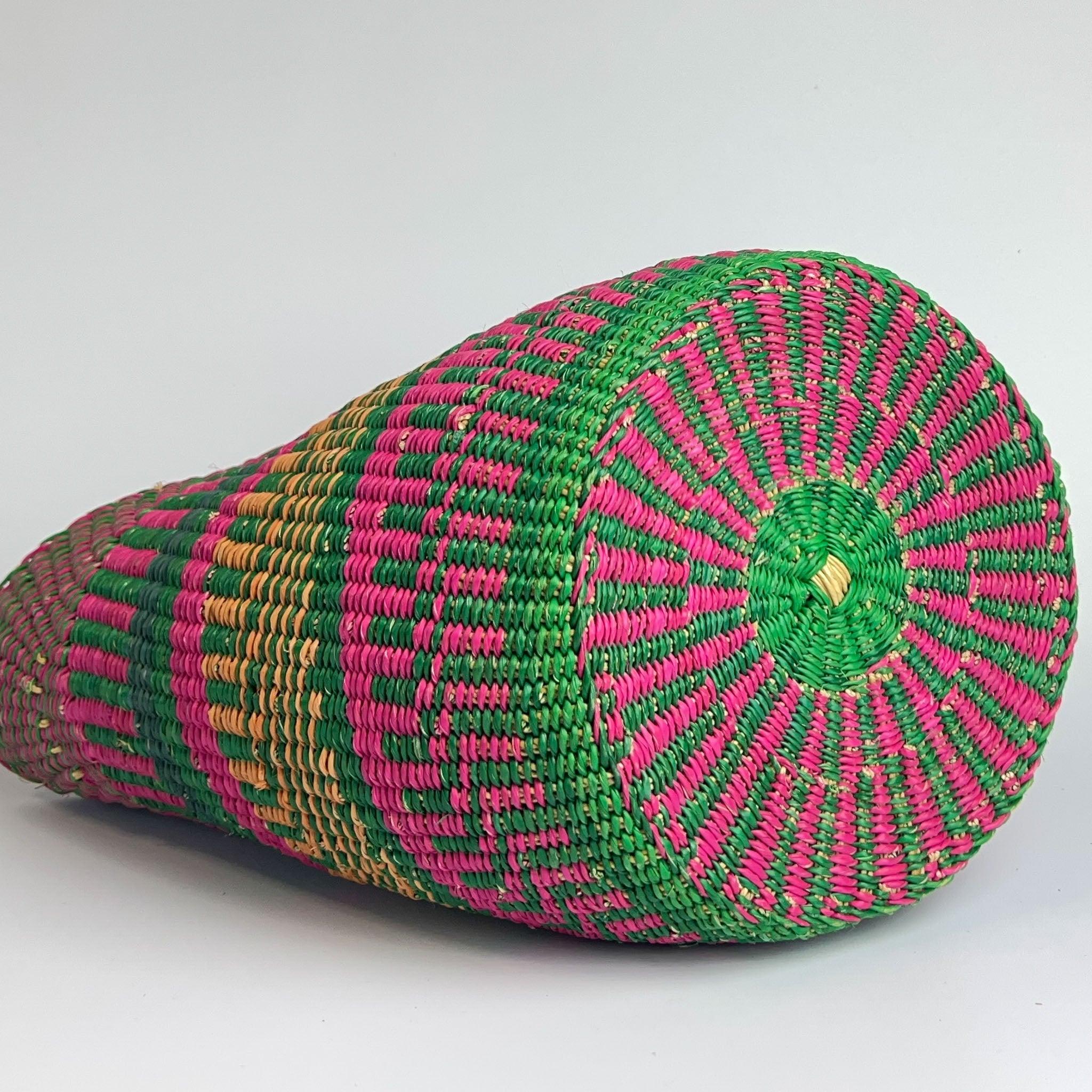 Traditional African shopping basket on it's side to show the intricate design and green  and pink colours of the base.