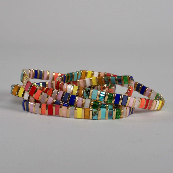 Cluster of flat Miyuki Glass bead bracelets in colourful rainbow colours, against a plain background