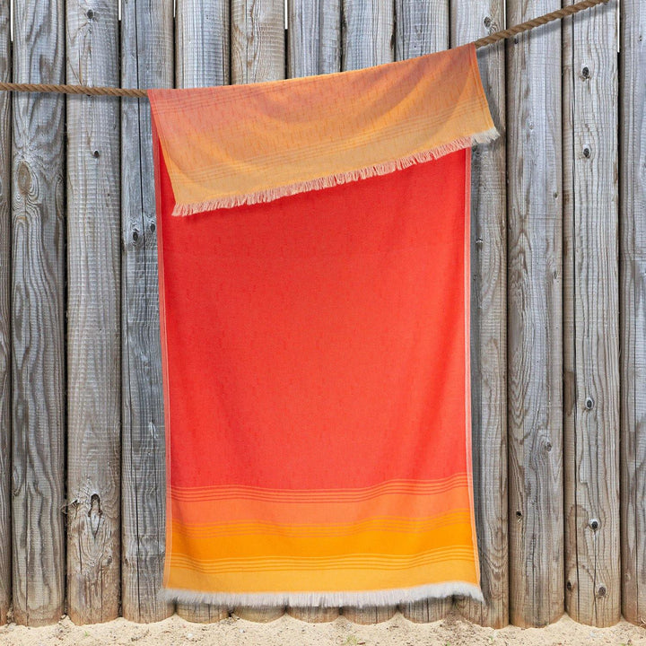 Sunset Beach towel hangs from a rope, showcasing its colourful design with one edge folded over, ready for a day at the beach.
