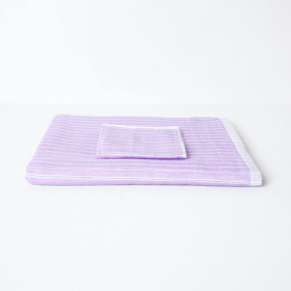 Baby bath towel folded flat with folded flannel.  The towel is lilac with a stripe design. 