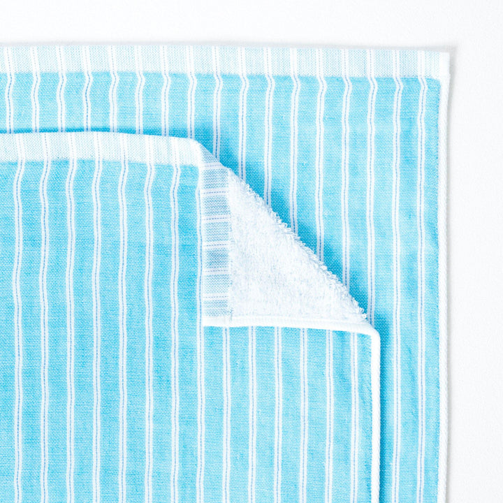 Close up of a turquoise and white stripe towel, with one corner turned down to show the soft terry pile on the reverse of the towel.