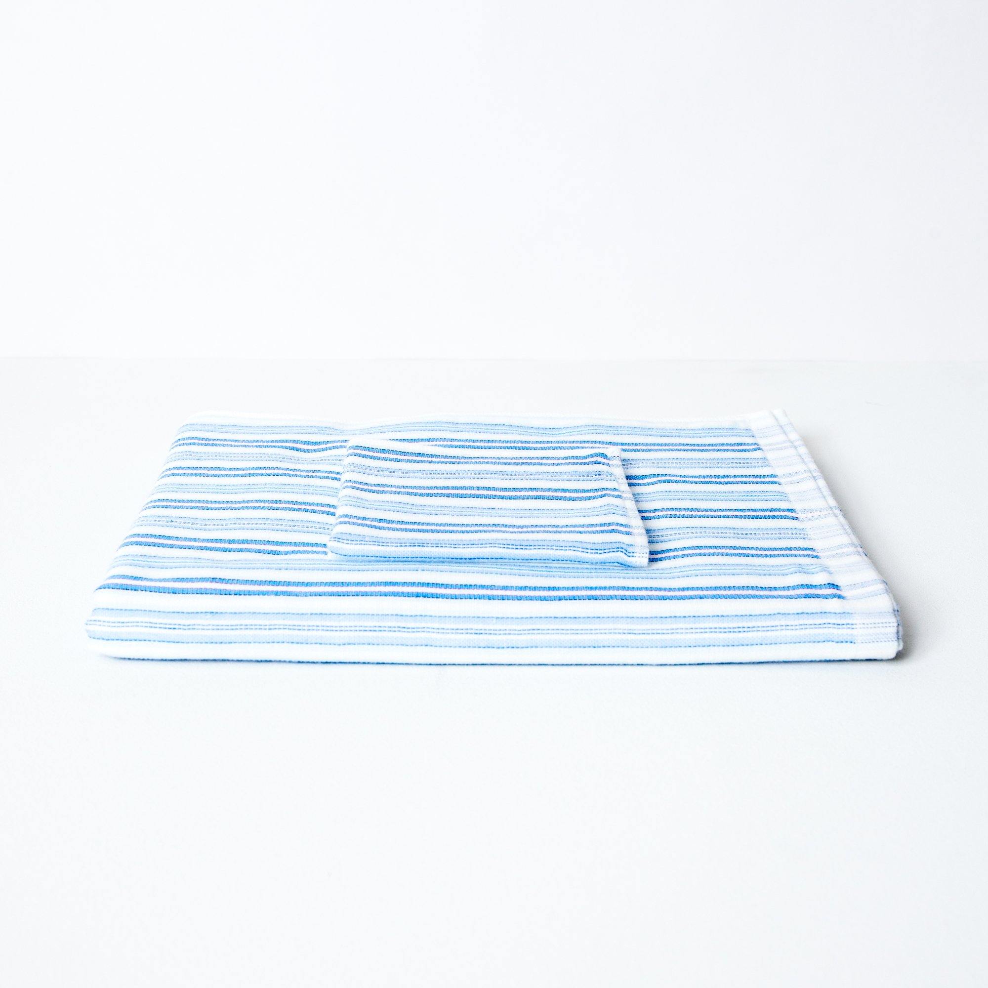 A striped towel with tones of blue, neatly folded with a coordinating flannel on top.