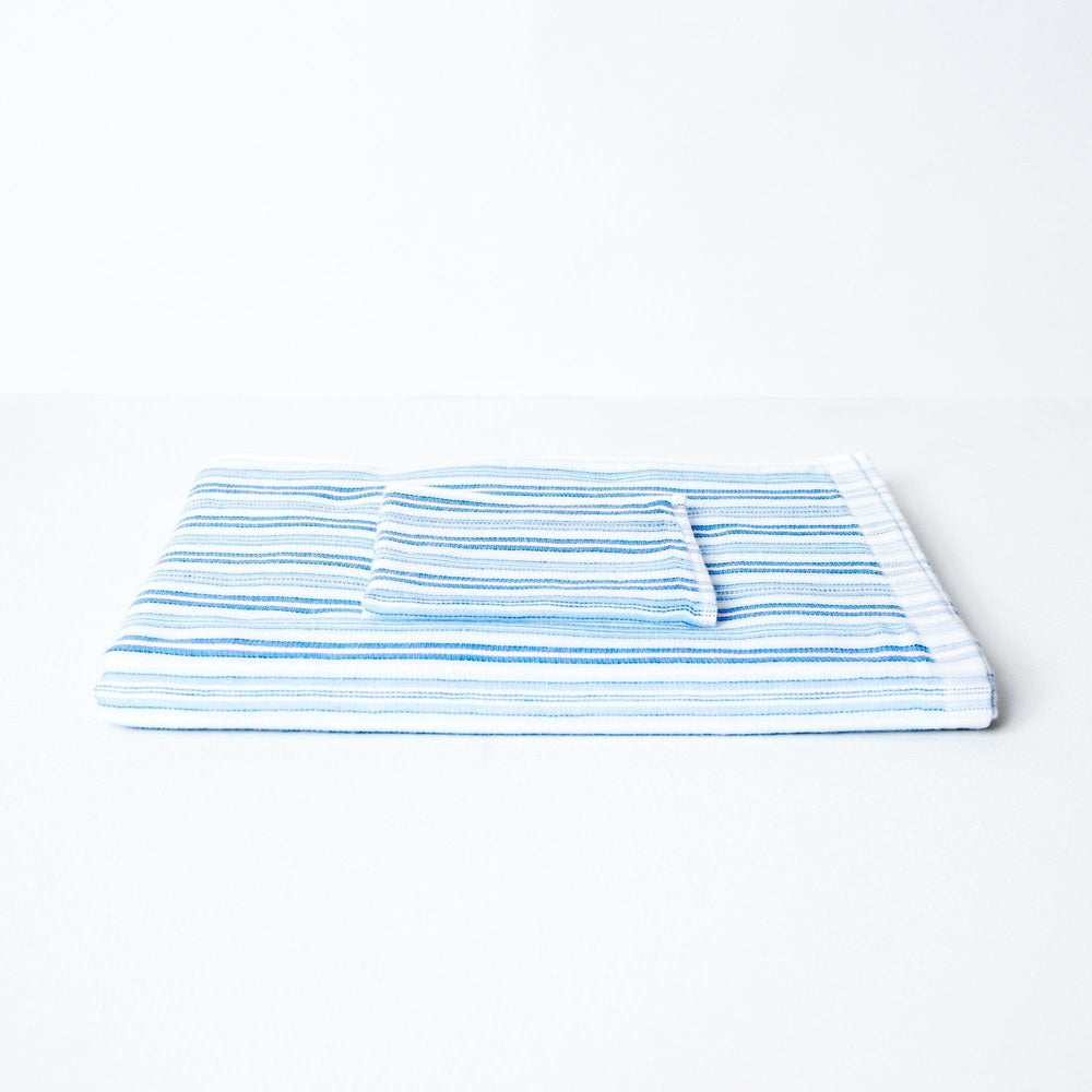 A striped towel with tones of blue, neatly folded with a coordinating flannel on top.