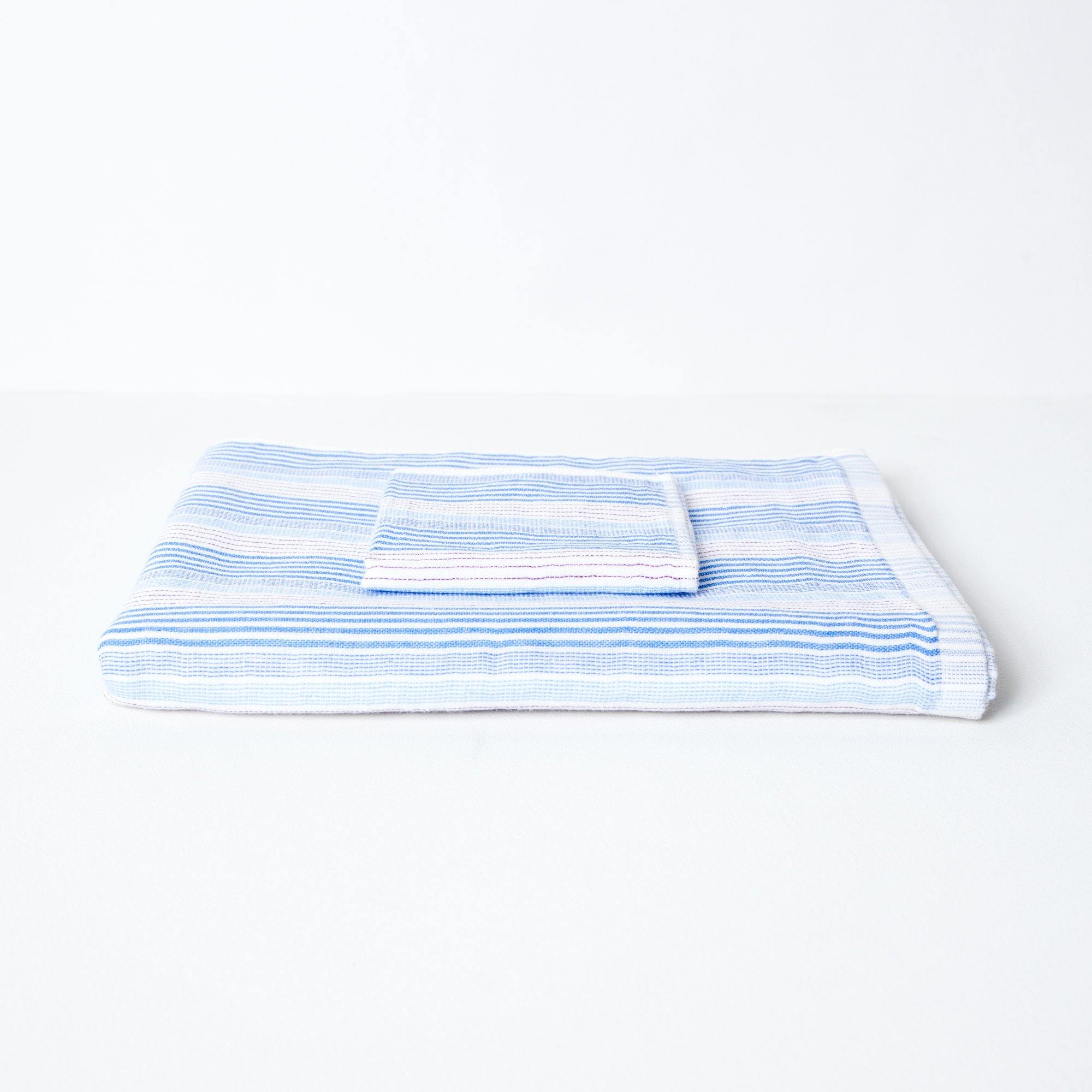 A striped towel with tones of blue and red, neatly folded with a coordinating flannel on top.