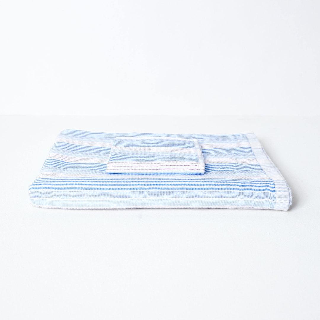 A striped towel with tones of blue and red, neatly folded with a coordinating flannel on top.