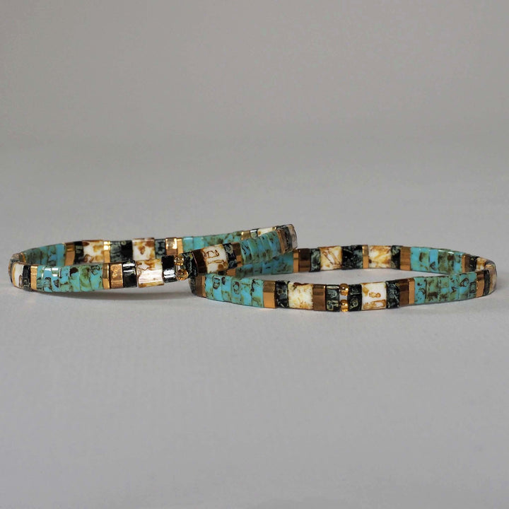 Couple of turquoise, gold and black design Miyuki Glass Bead bracelets, against a plain background