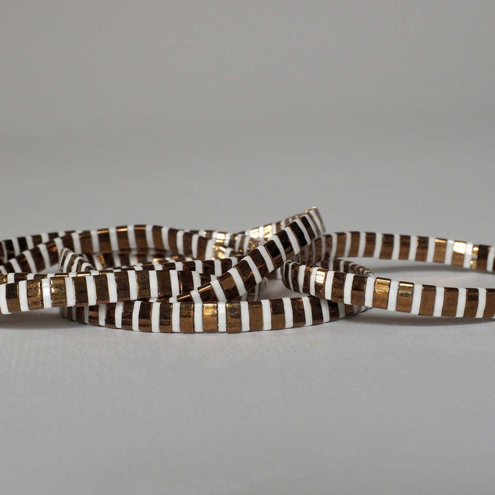 Elegant gold and white Miyuki Glass Bead bracelets stacked on top of each other, against a plain background