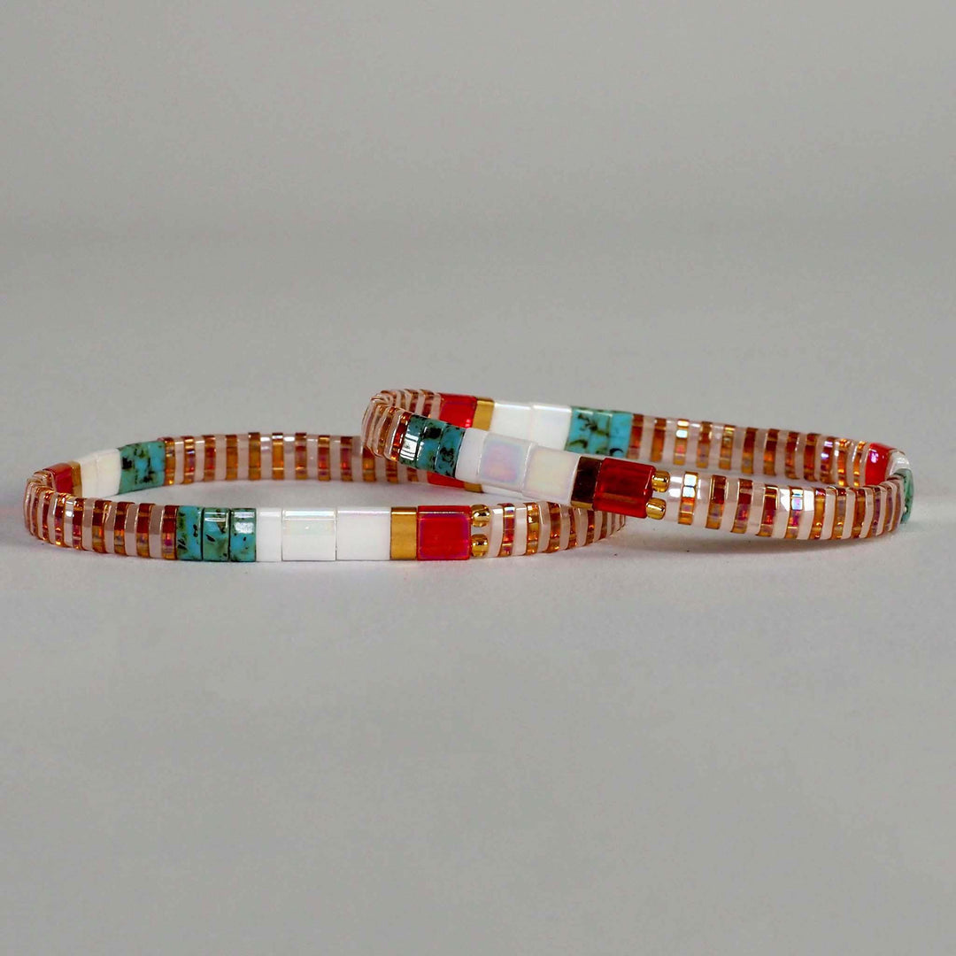 Two Miyuki Glass Bead flat bracelets, in red turquoise, gold and white design, against a plain background
